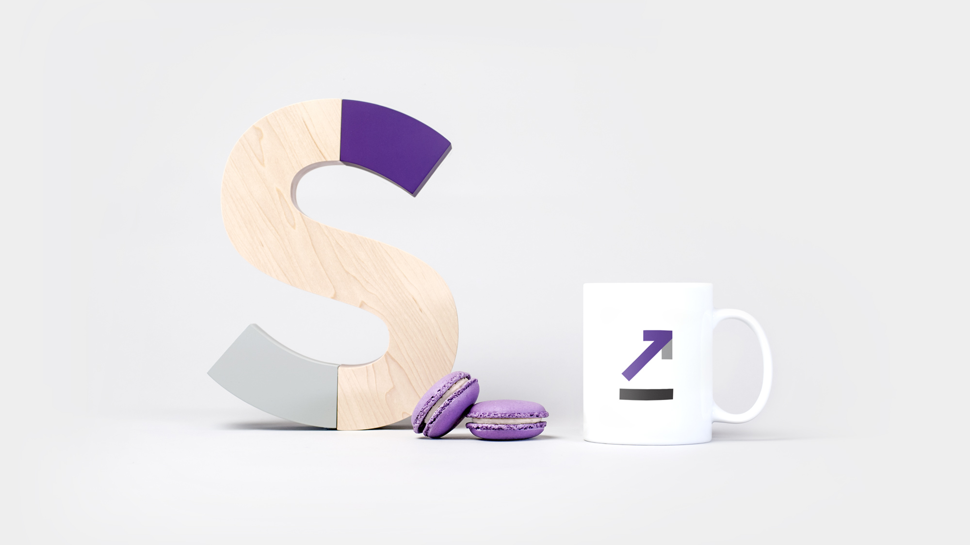The Stride Property S logo made out of wood alongside a mug with an icon on it and two purple macarons